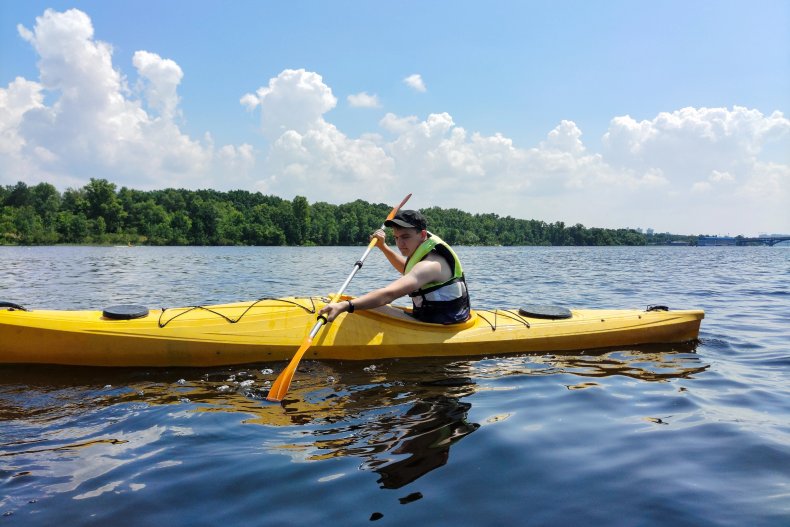 A young Caucasian guy is practicing kayaking on the river against the background of the sky and the distant shore. Sports and an active lifestyle