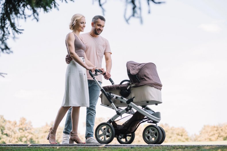 Unos padres felices con sus hijos y un cochecito dando un paseo por el parque