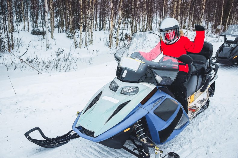 Una mujer conduce una moto de nieve en invierno en un bosque nevado