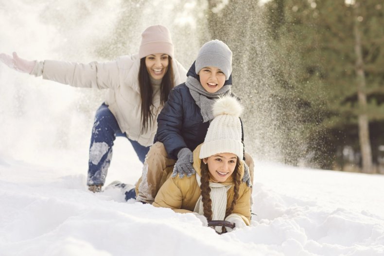 Una madre y sus hijos se divierten bajando por un tobogán en un parque de invierno